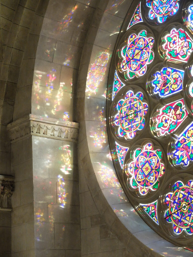 Detail of a colorful stained-glass window with its reflected light on stone building