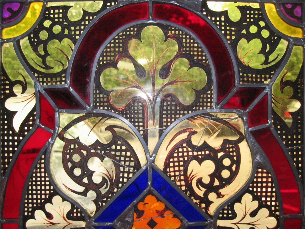 Detail of ornamental stained-glass panel with abstract plant decorations in red, blue, green, and yellow, with lead edges.