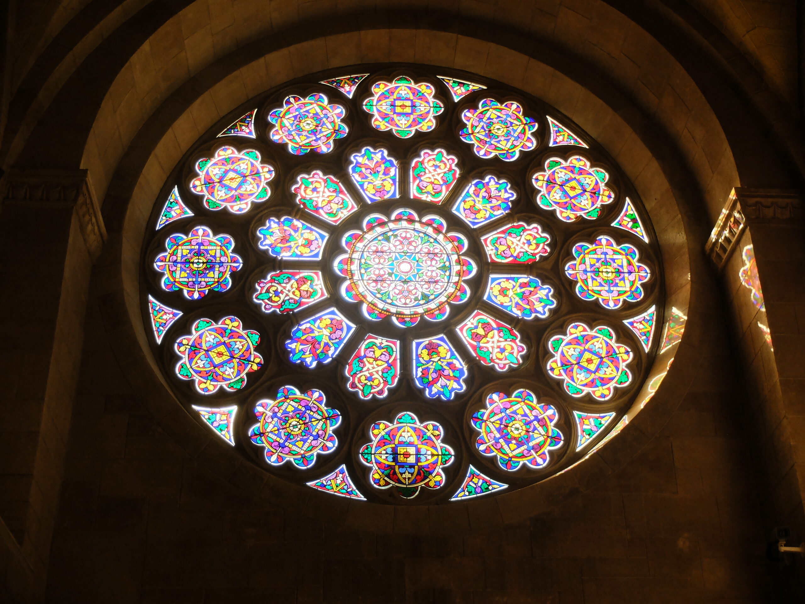 Large, round, colorful stained-glass window with light shining through onto building interior