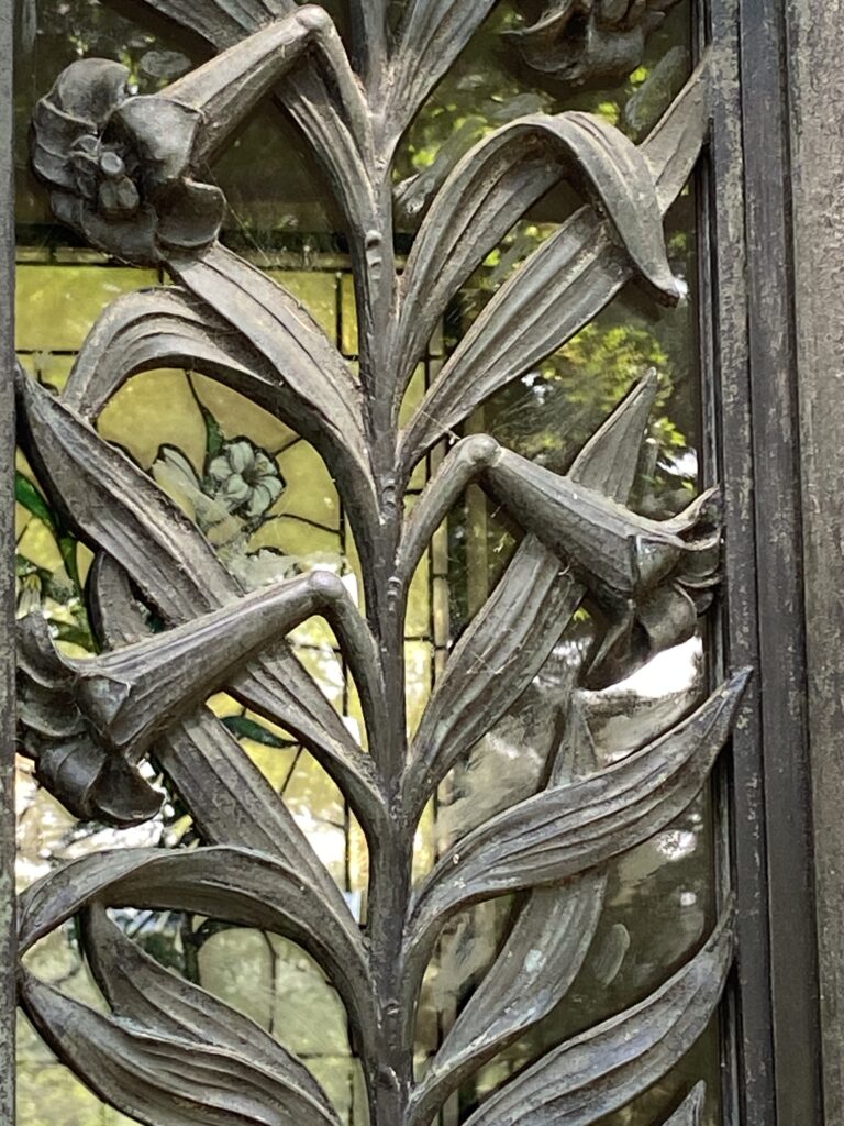 Lilies wrought in iron on a door with stained glass window in the background